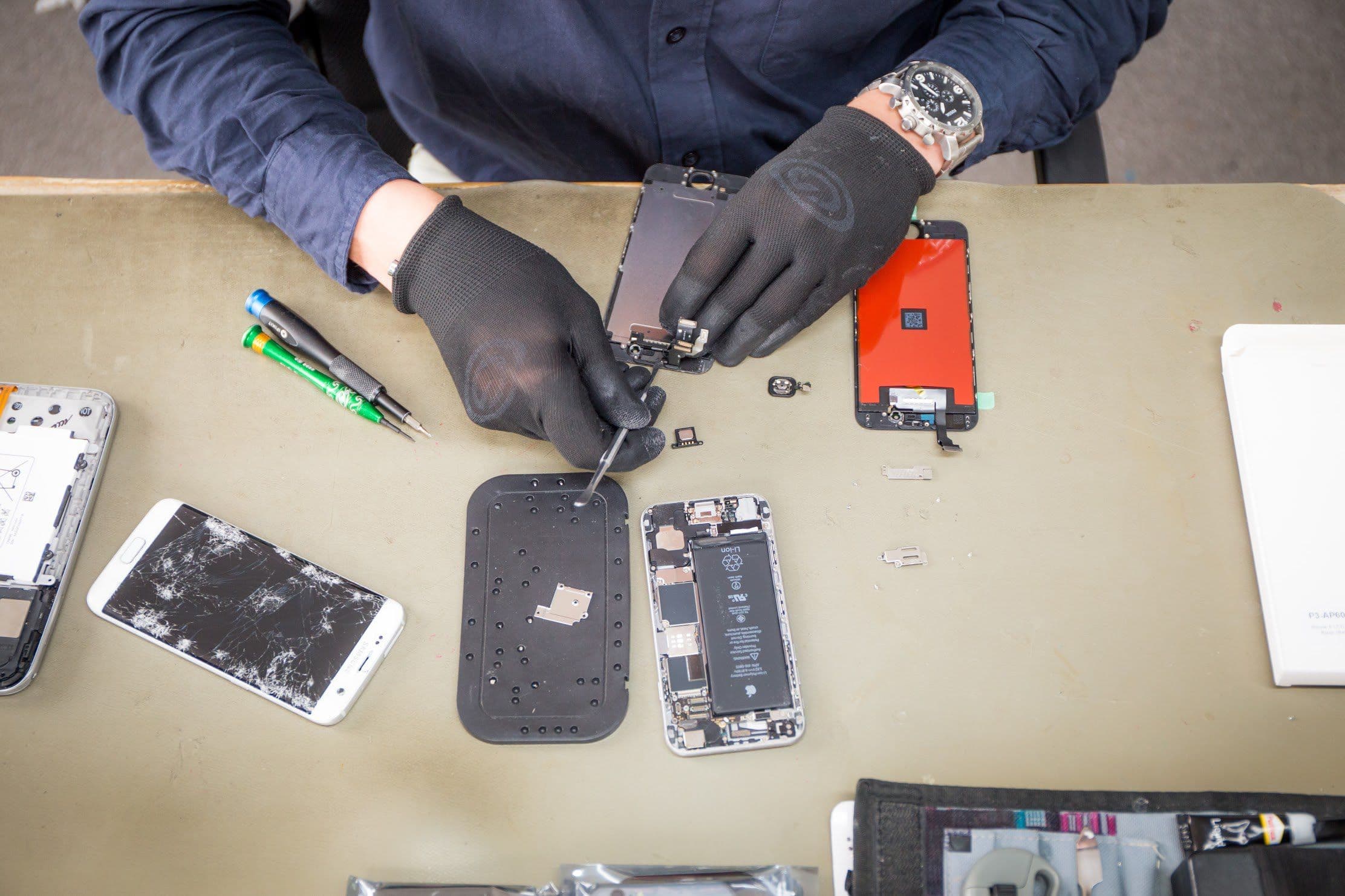 Reparateur haalt een telefoon uit elkaar op de werkbank, met onderdelen en gereedschap eromheen